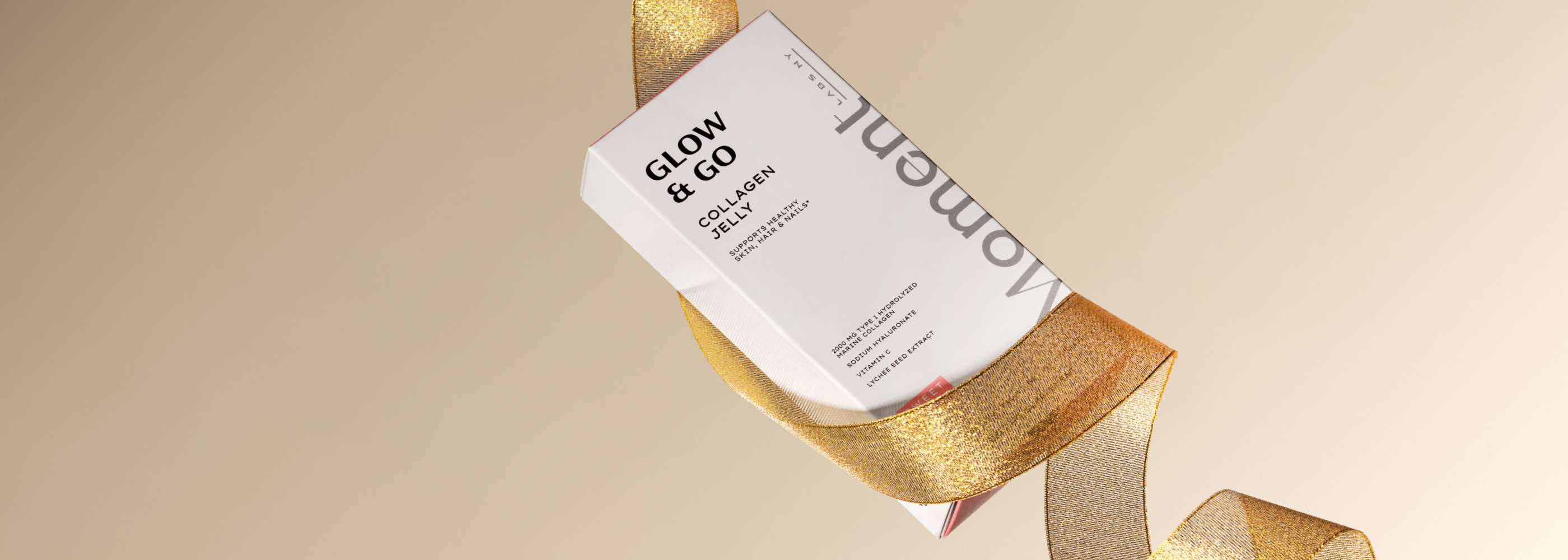 Gold and white cosmetic packaging with 'Moment Labs NY' branding on a beige background
